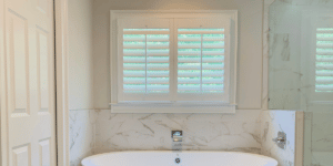 Hardwood Plantation Shutters with 3.5 inch louvers let a little light in above a marble-trimmed white bathtub in Sandy Springs, GA