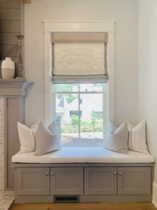 Classic, gray Roman Shades roll halfway down a single window in a luxurious, white great room in Atlanta, GA