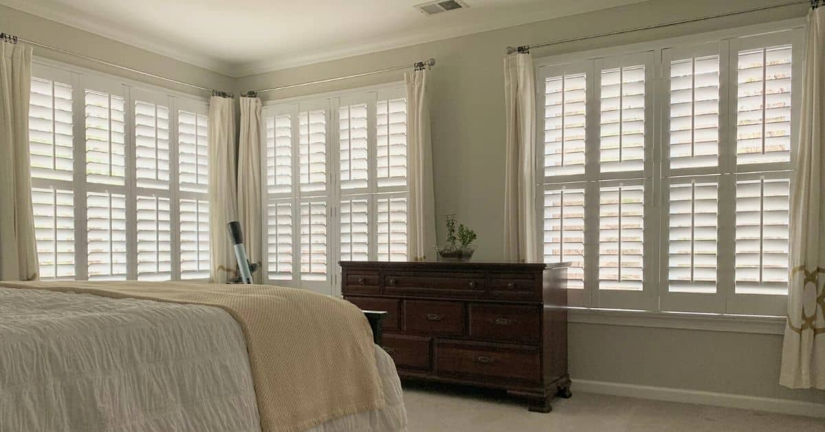 Hardwood Plantation Shutters featuring split tilt rods gently filter light into a dimly lit and spacious bedroom