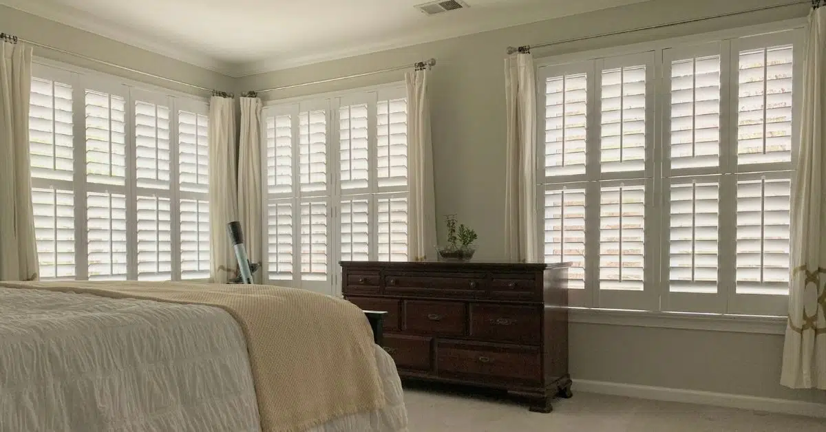 Hardwood Plantation Shutters featuring split tilt rods gently filter light into a dimly lit and spacious bedroom