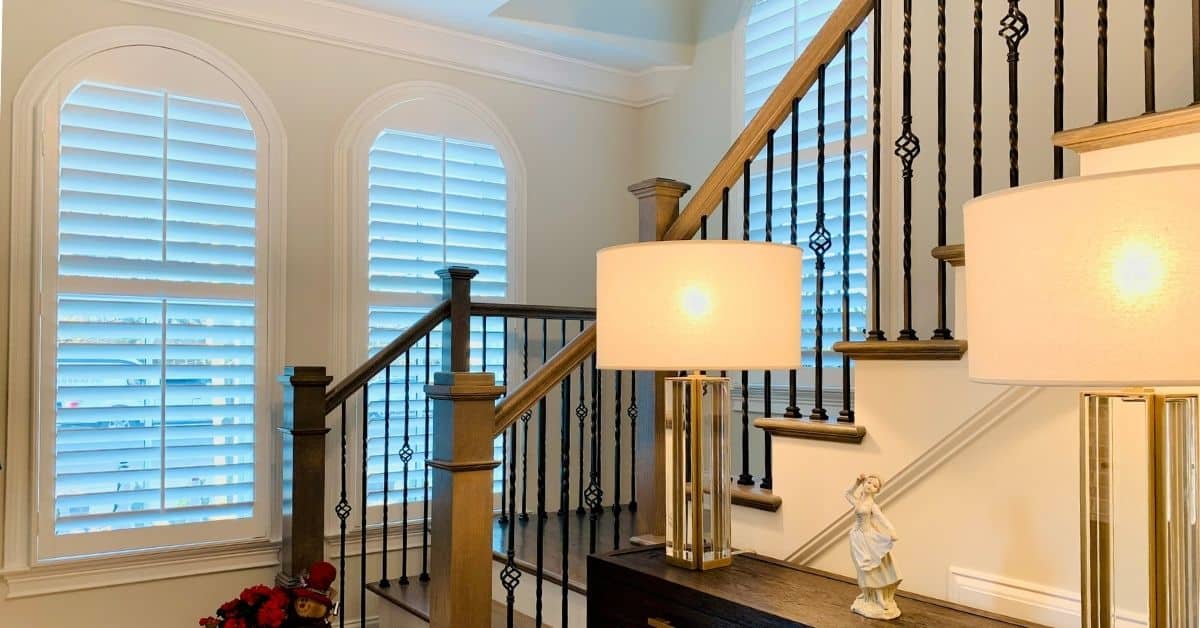 Hardwood Plantation Shutters featuring 3.5 inch louvers and split tilt rods, designed with a lazy arch, meaning an arch that less than half a circle, at the landing of wooden stairs in a Nashville, TN townhome