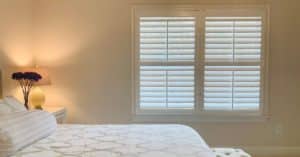 Hardwood Plantation Shutters featuring 3.5 inch louvers divider rails in a white, dimly lit bedroom in Roswell, GA