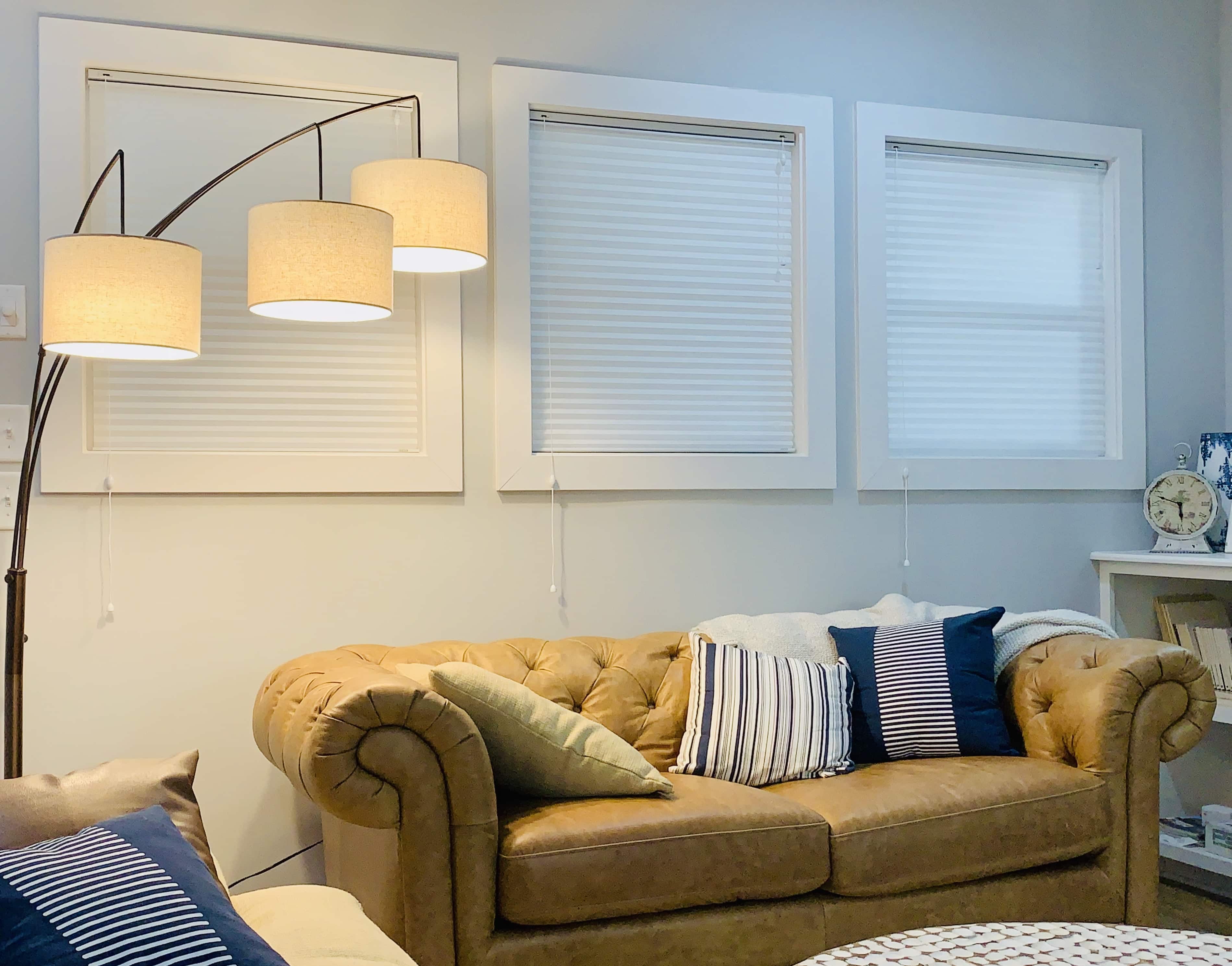 Three windows covered by white cellular shades above a brown sofa