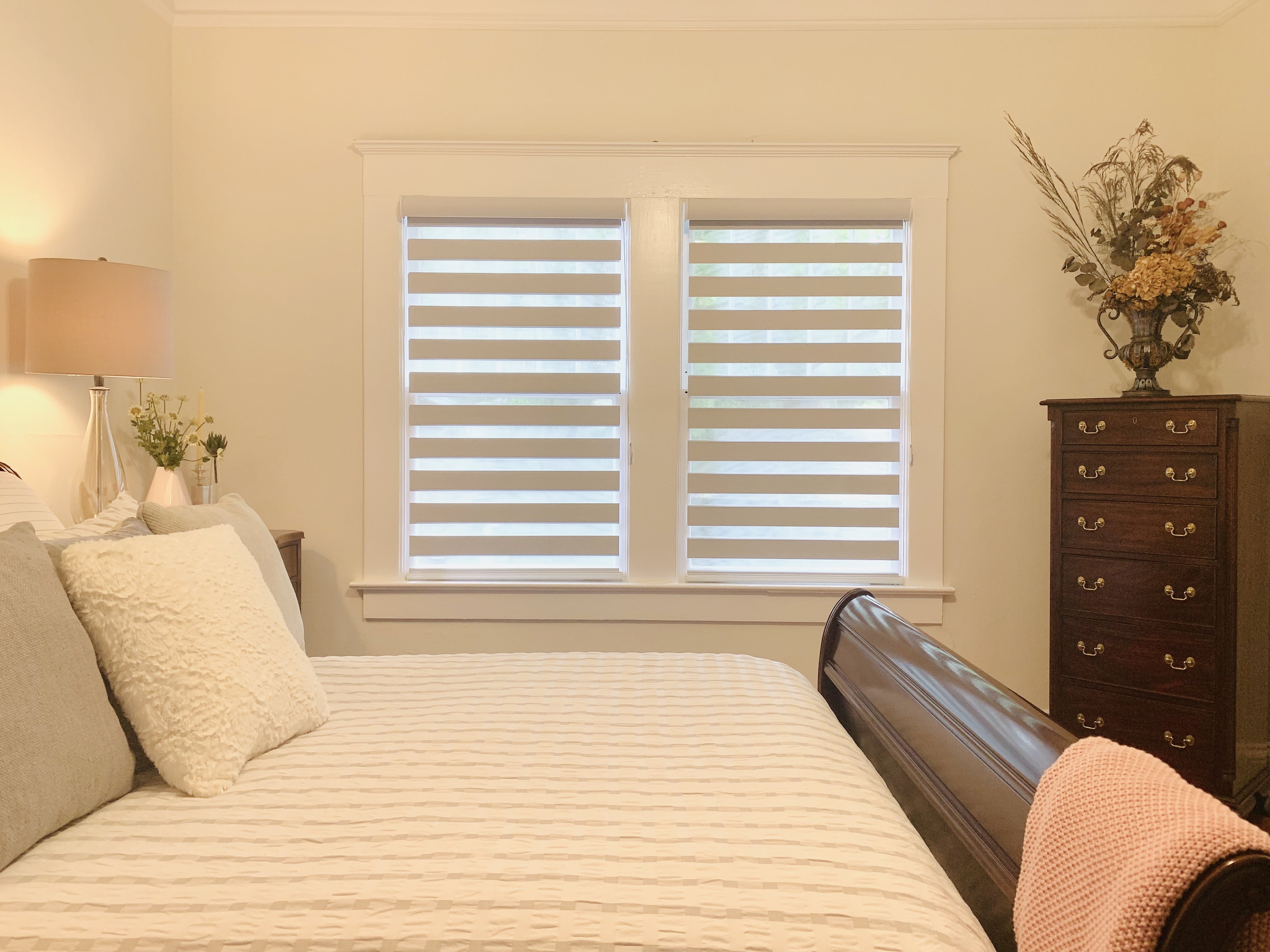 Layered shades in their open position on two windows in a bedroom