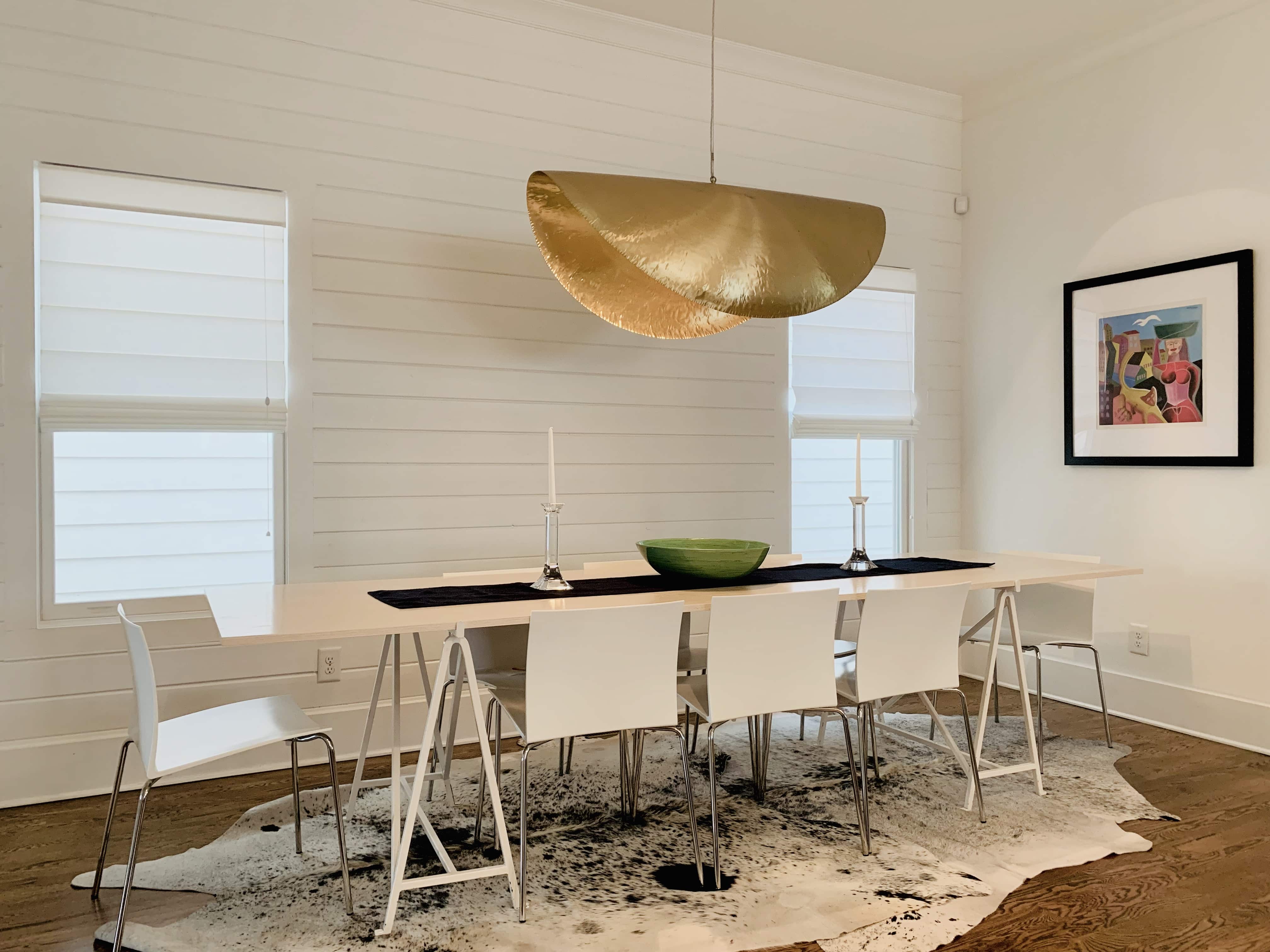 Two roman shades lowered halfway on two large windows behind a dining room table