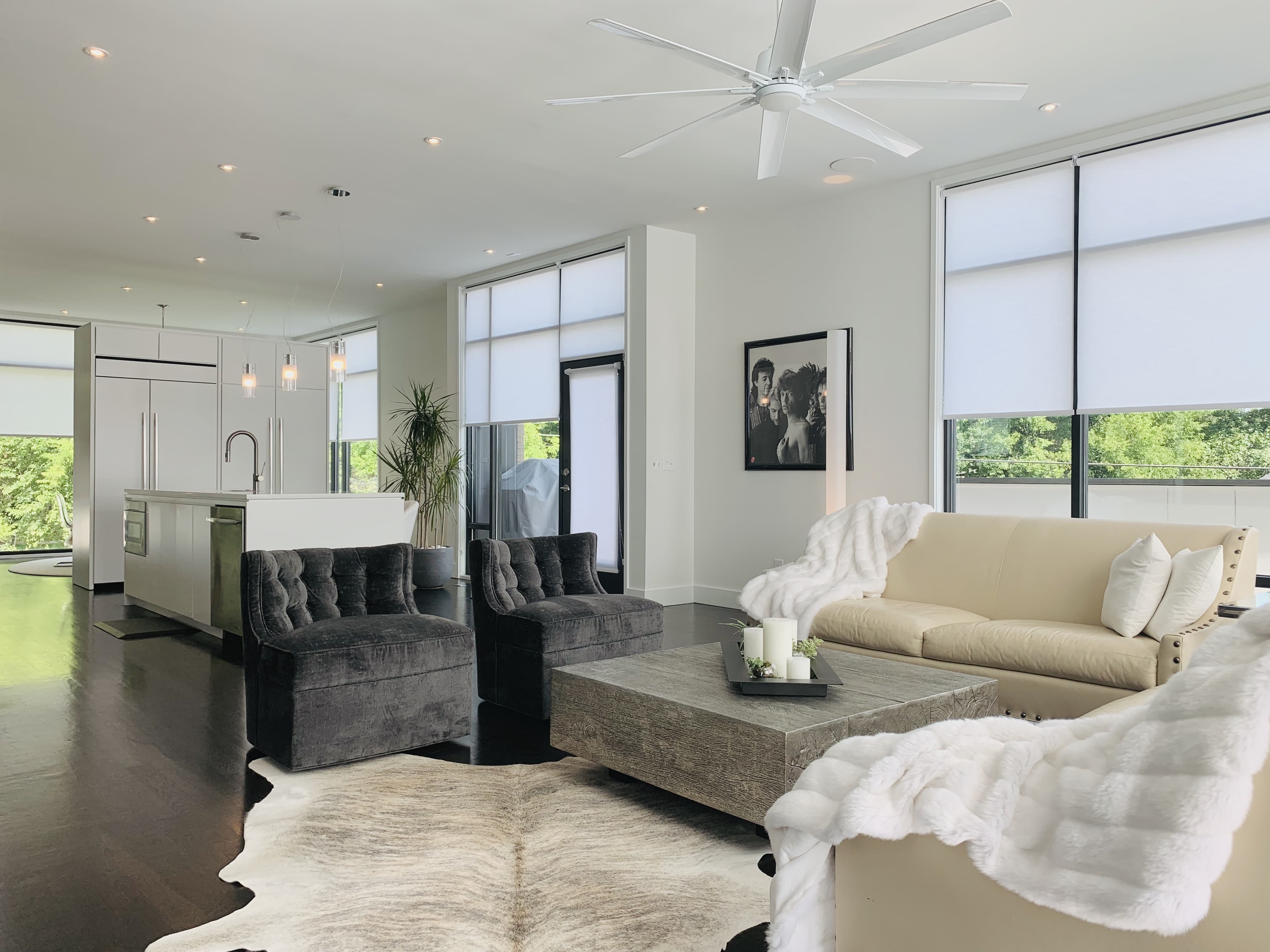 White roller shades filter light on five large windows in a kitchen and living room area