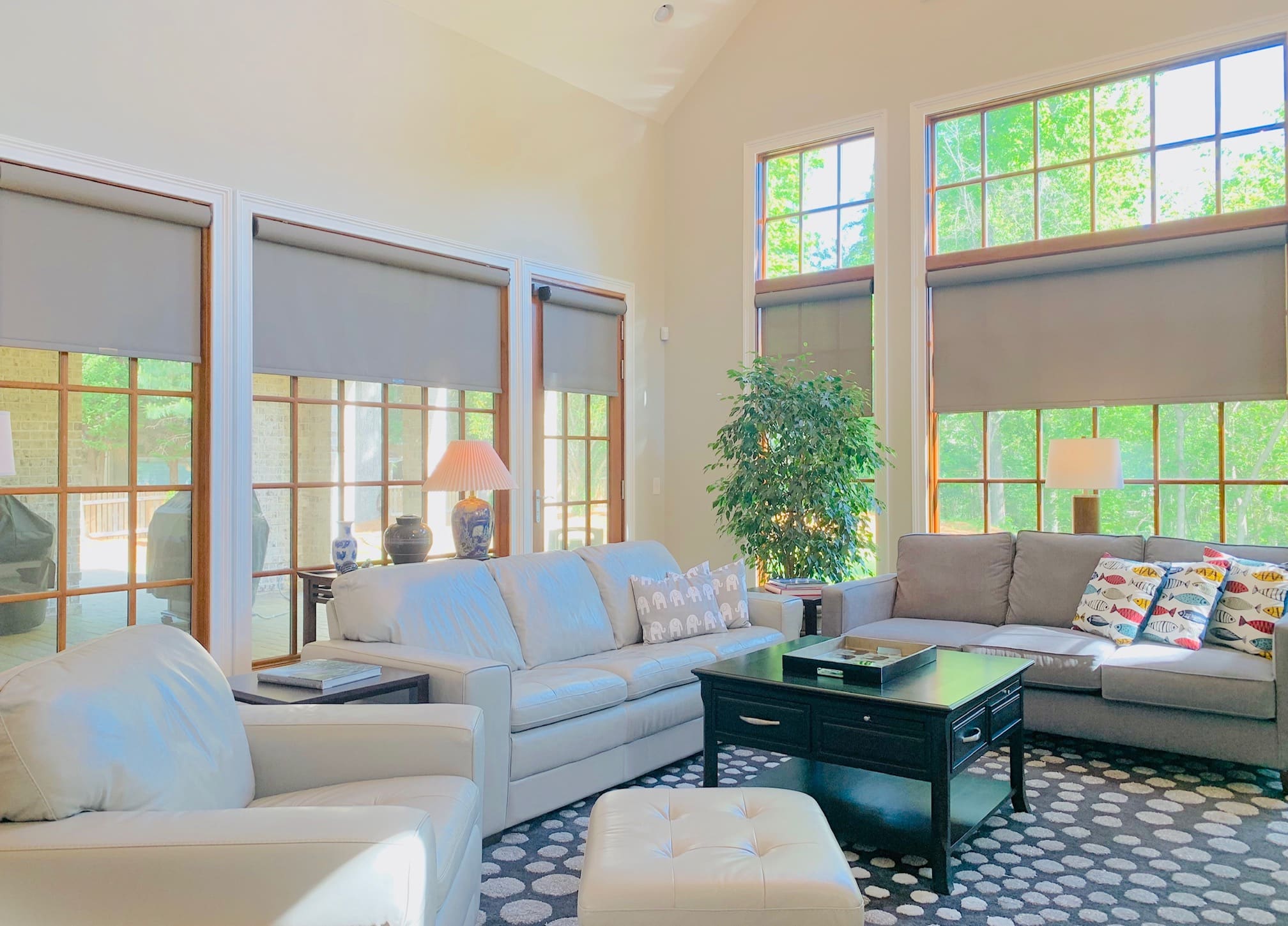 Five grey roller shades cover five large wood-trimmed windows in a spacious living room