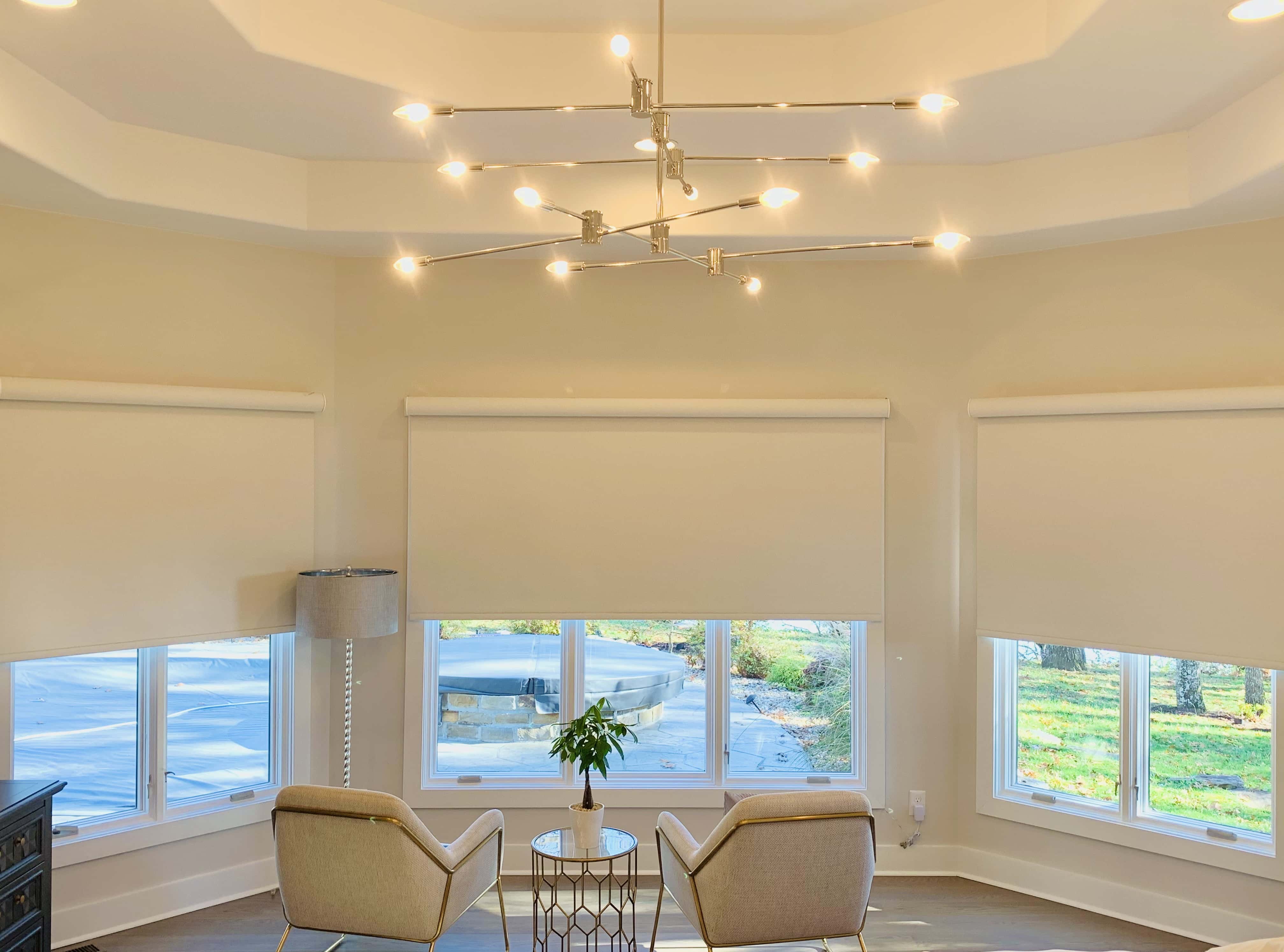 Three large windows partially admit light into a sitting area with two chairs on either side of a small table