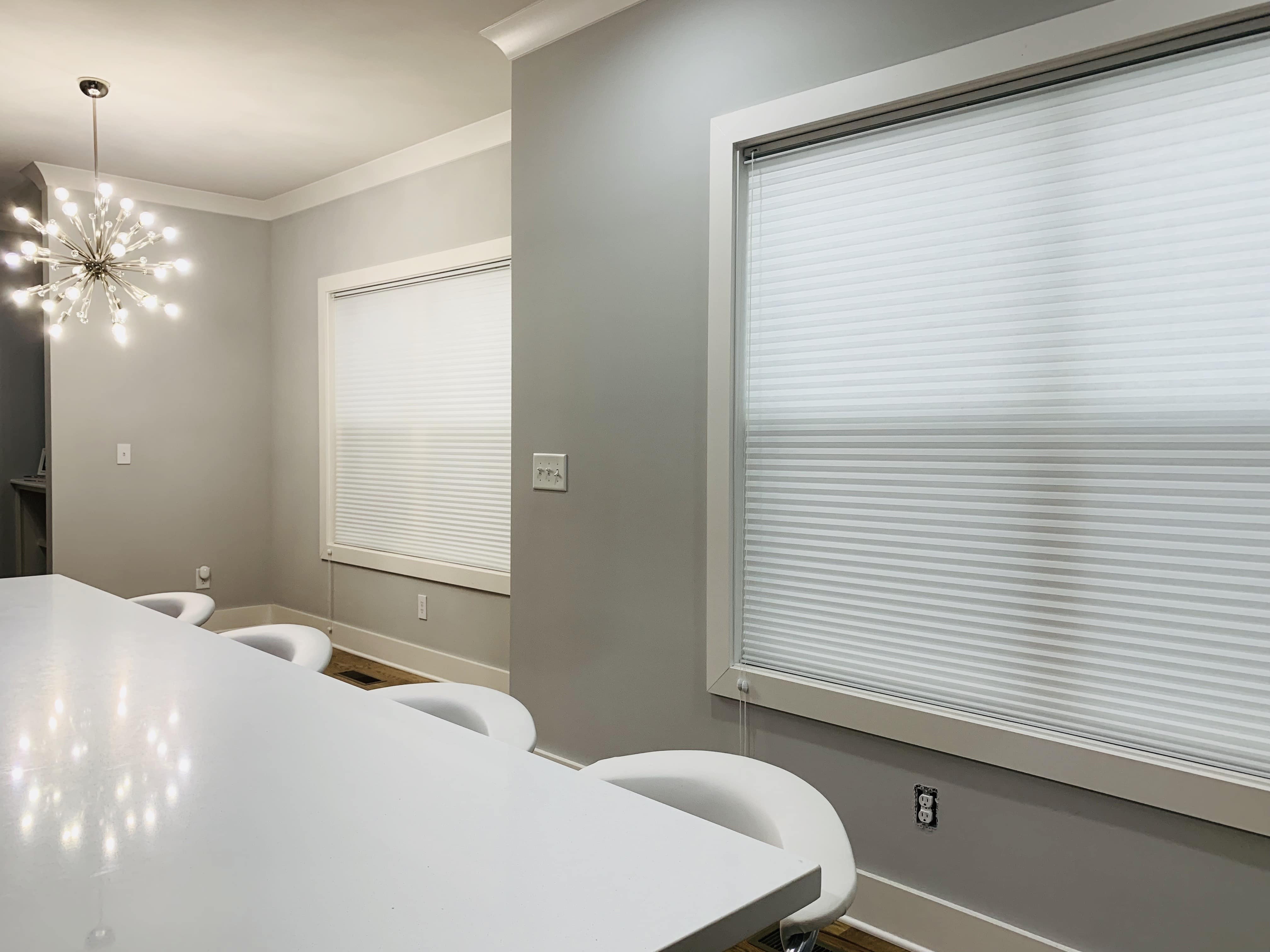 Two large windows covered by cellular shades behind a counter and four stools