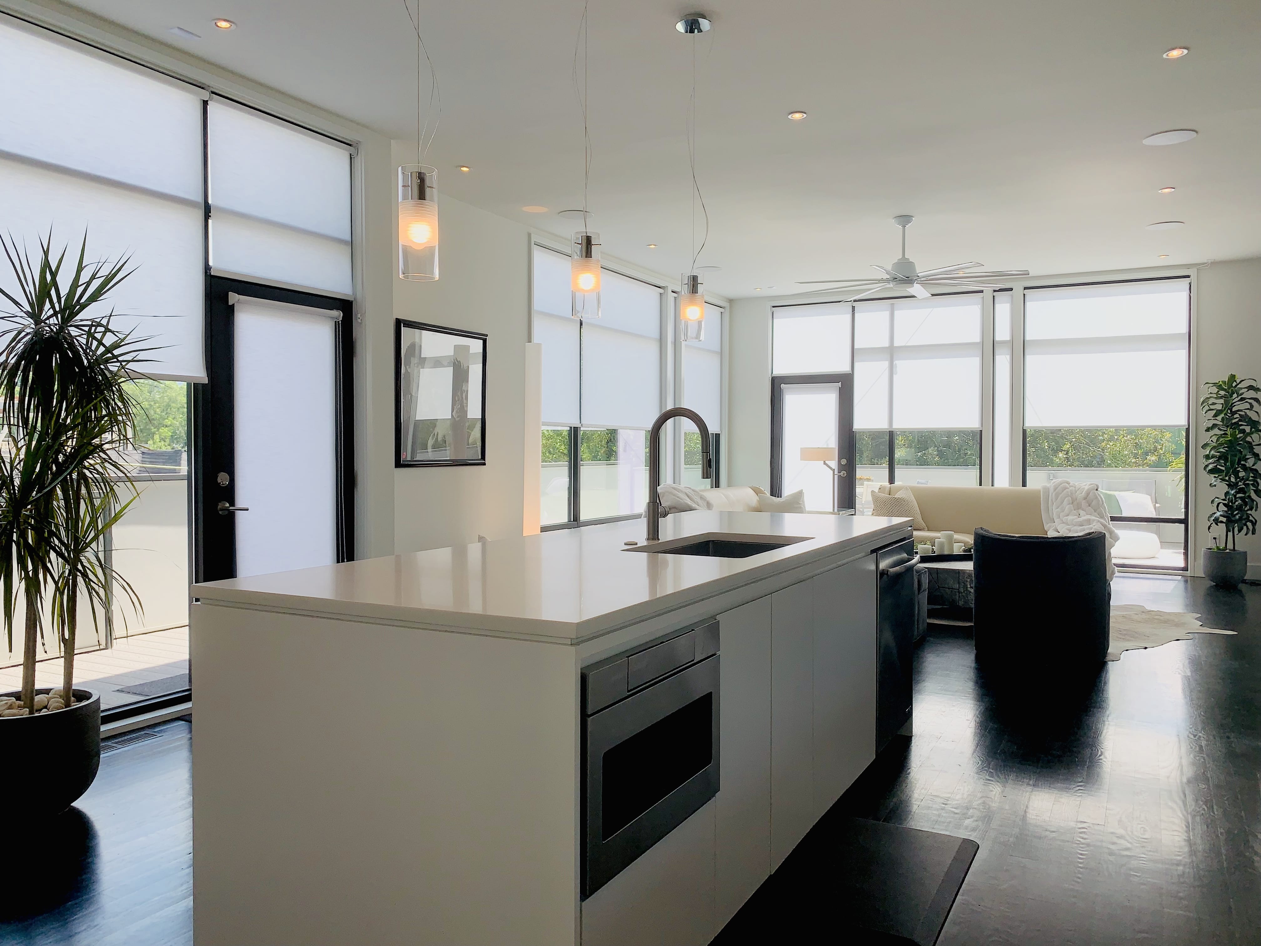 White roller shades partially cover large windows in an open kitchen and den area