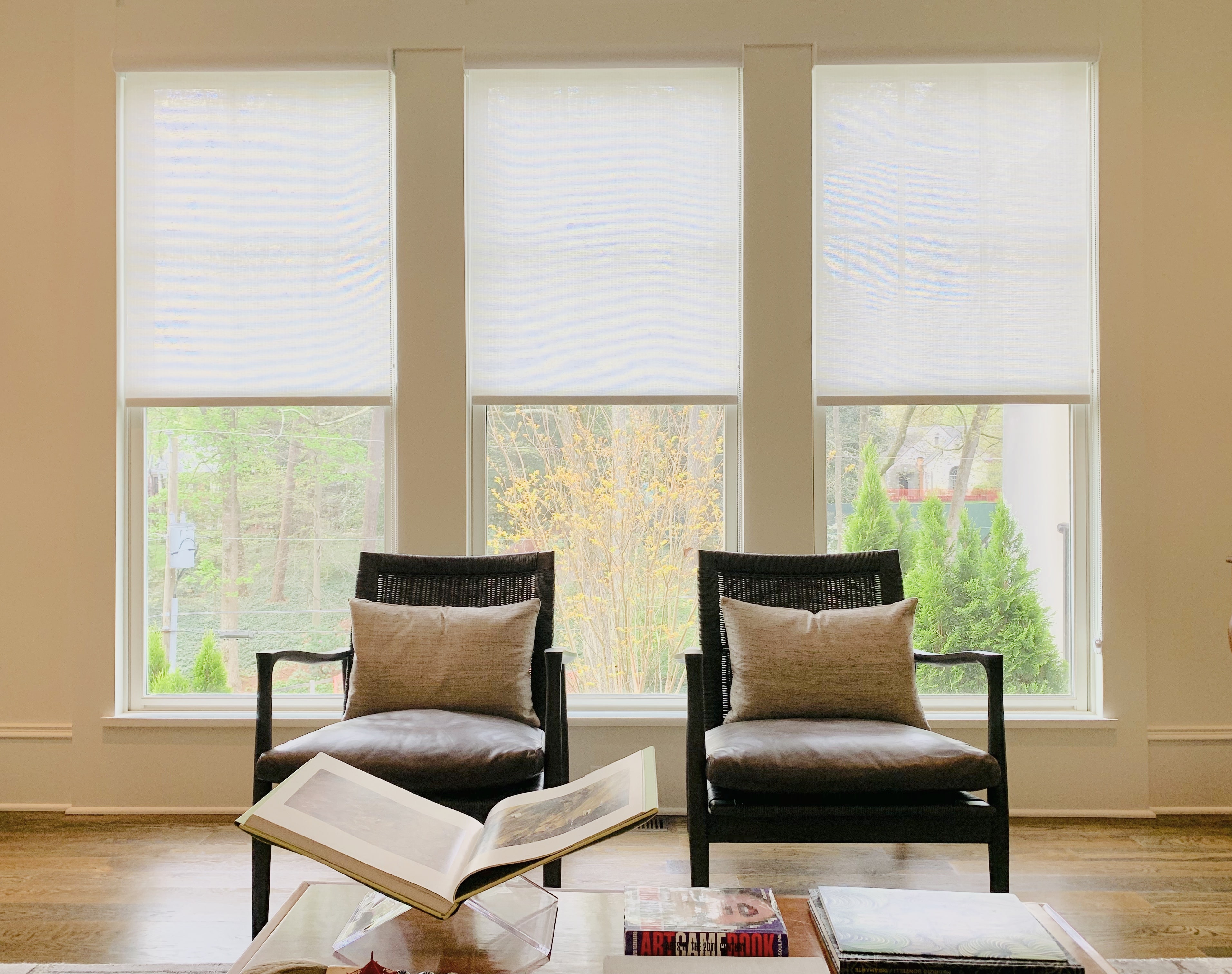 Three white, woven shades reveal a sunny day behind three large windows behind two chairs